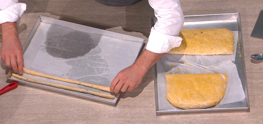 In una ciotola, mettiamo la farina tipo 0, il lievito fresco sbriciolato, il malto, gran parte dell'acqua e cominciamo a lavorare con un cucchiaio. Ad impasto formato, inseriamo il sale, l'acqua rimasta e lavoriamo ancora per qualche minuto. A questo punto, aggiungiamo le olive nere tritate al coltello (possiamo evitarle) ed impastiamo fino ad inglobarle all'impasto. Copriamo e lasciamo riposare per 10 minuti a temperatura ambiente.
Schiacciamo l'impasto con le mani e lo 'paniamo' nella farina di mais per polenta. Posizioniamo l'impasto su una teglia, lo copriamo e lo lasciamo riposare per 1 ora al caldo.
Tagliamo l'impasto a fette, quindi tiriamo ciascuna fetta tra le mani, allungandola e creando i grissini. Li disponiamo su una teglia con carta forno, li copriamo e li lasciamo riposare 10 minuti a temperastura ambiente.
Li cuociamo in forno caldo e statico a 220° per 10 minuti; quindi a 200° per altri 10 minuti, con lo sportello del forno socchiuso.